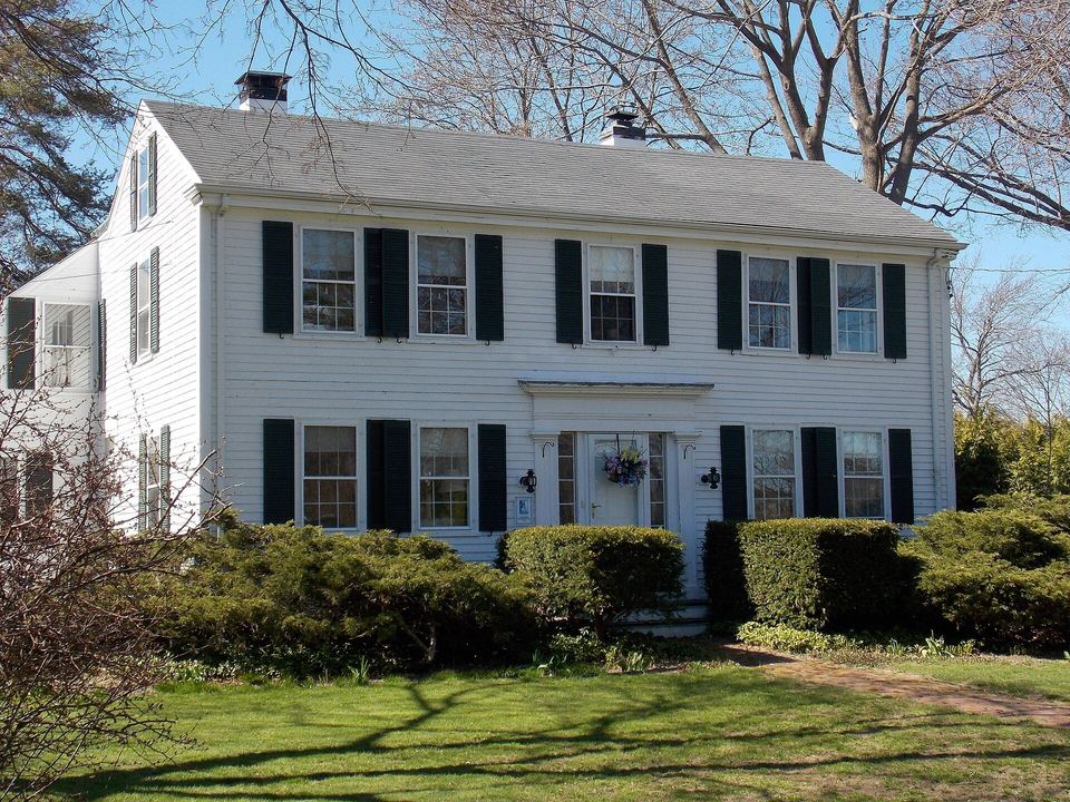 White two-story colonial house with black shutters, a center doorway and a green lawn